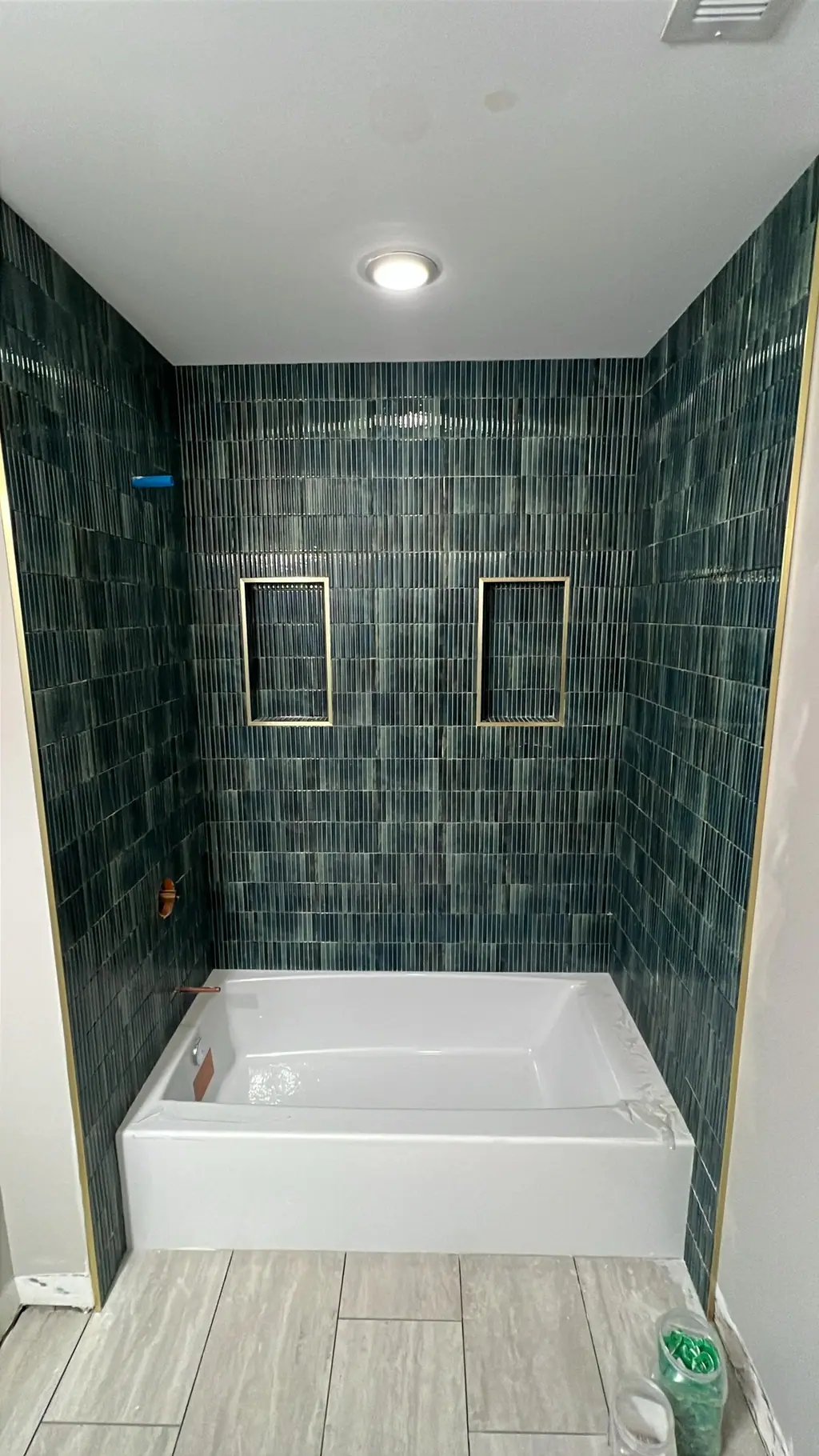 Tub surround finished in blue stacked tile with two brass-trimmed niches