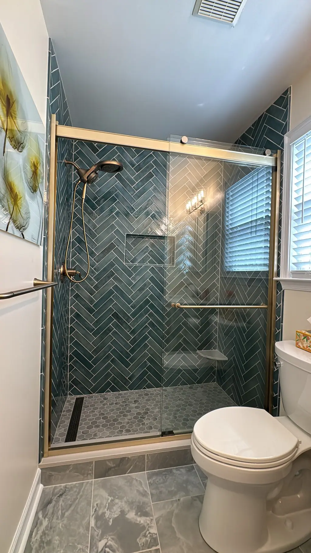 Walk-in shower with teal herringbone wall tile, niche and brass glass door