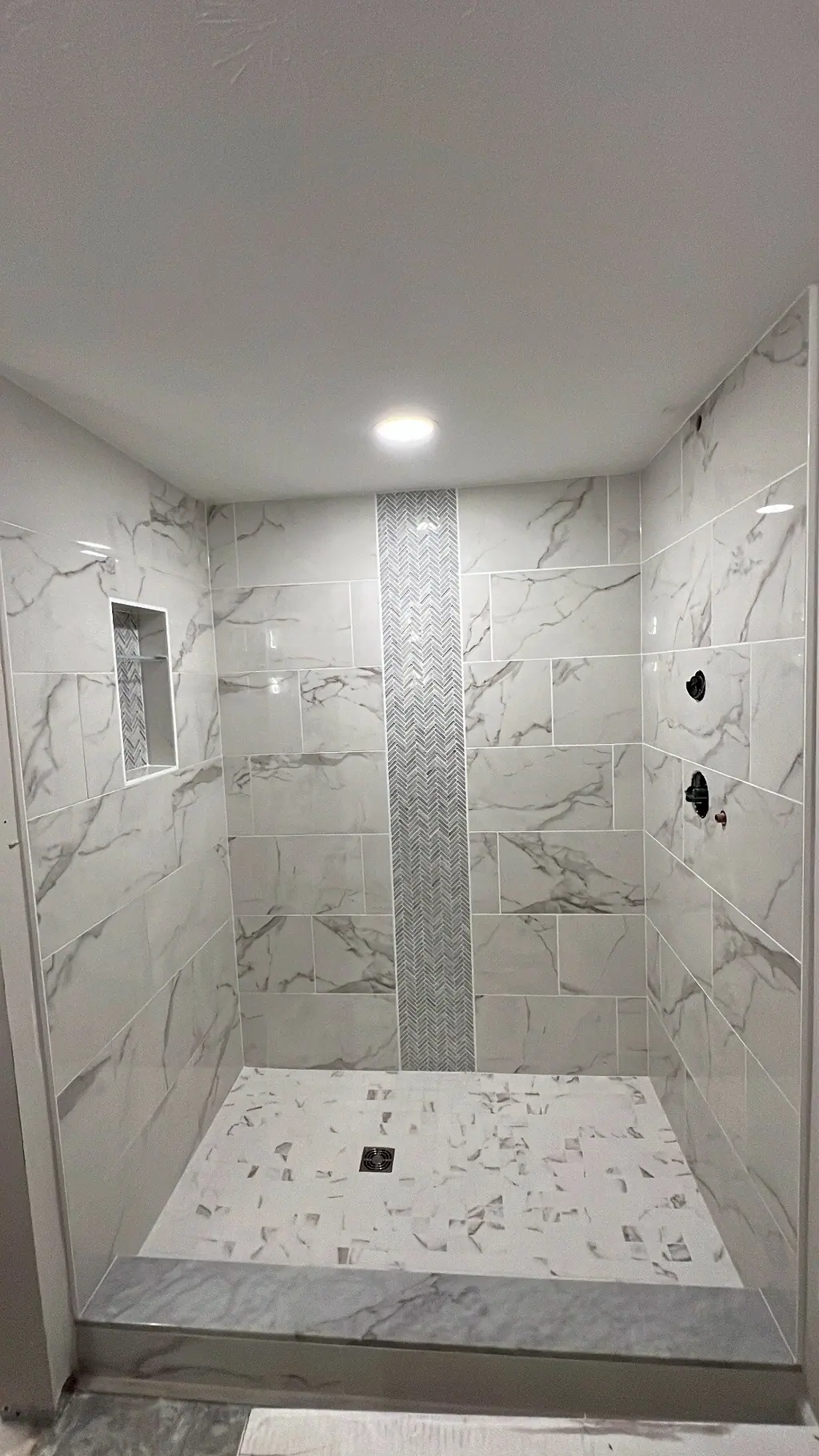 Marble-look shower with vertical herringbone accent strip and niche