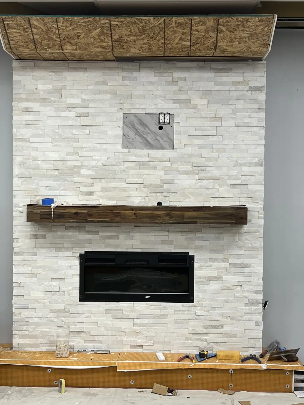 Stacked stone veneer fireplace wall with wood mantel